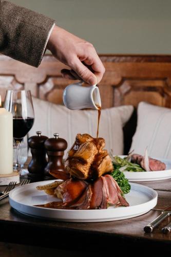 a person is pouring gravy on a plate of food at The Crown, Bildeston in Bildeston