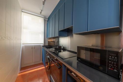 eine Küche mit blauen Schränken und einer schwarzen Mikrowelle in der Unterkunft Cornerstone, apartamento en Casco Viejo in Bilbao