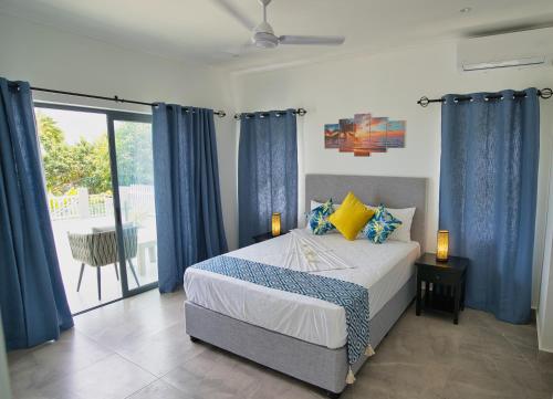 1 dormitorio con 1 cama con cortinas azules y balcón en Sunset Haven Villa en Beau Vallon