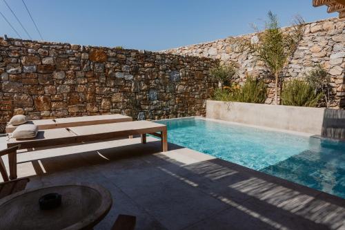 a swimming pool with a bench next to a stone wall at Oliving Mykonos Luxury Suites in Klouvas