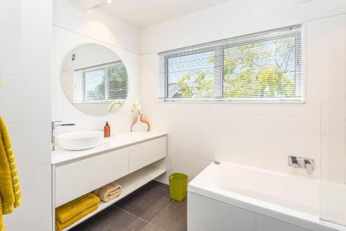 a white bathroom with a sink and a mirror at Retro Living - Lush Garden in Christchurch