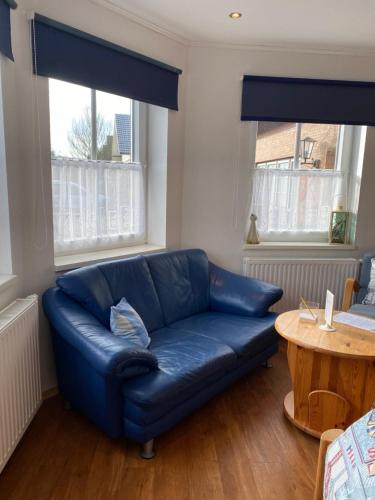 a blue leather couch in a living room with two windows at Schumacher's Landhaus - Bücherhotel in Friedeburg