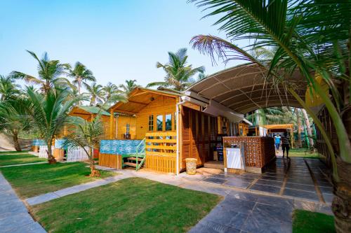 a small yellow house with a porch and palm trees at orange sky beach bungalow in Agonda