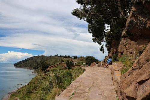 a person sitting on a stone path next to the water at WHITE SAND Taquile Lodge in Huillanopampa