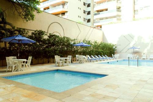 uma piscina com mesas, cadeiras e guarda-sóis em Apartamento aconchegante. no Rio de Janeiro