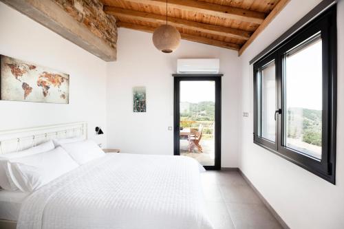 a bedroom with a white bed and large windows at Monopati Eco Villas in Raches