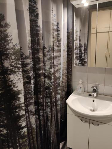 a bathroom with a sink and a shower curtain with trees at Hilla Apartments in Rovaniemi