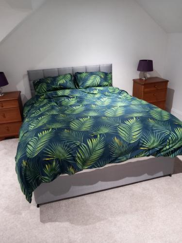 a bed with a blue comforter with green leaves at Couple's Retreat-West Kilbride in Seamill