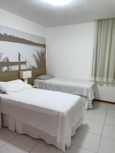 two beds in a room with white walls at Apartamento Iloa residence in Barra de São Miguel