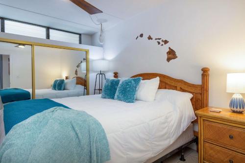 een slaapkamer met een bed met blauwe kussens en een spiegel bij Kihei Akahi C-608 - Stunning Ocean Views, AC! in Wailea