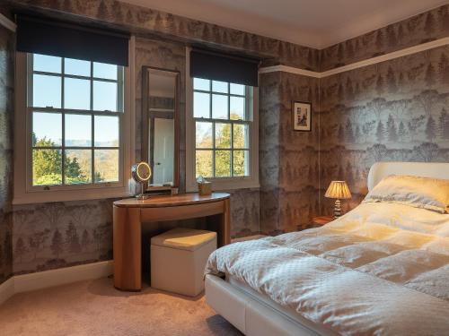 a bedroom with a bed and a desk and windows at Orrest Howe in Windermere
