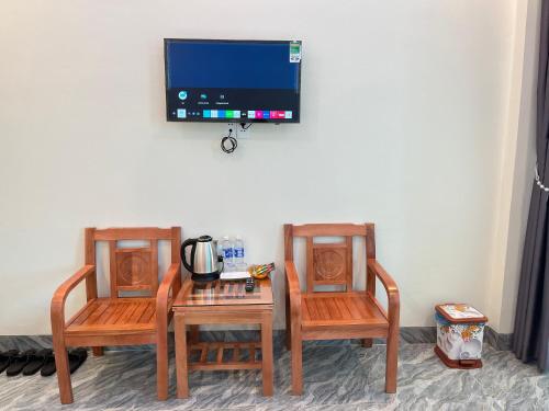 twee stoelen en een tafel met een tv aan de muur bij NHÀ NGHỈ ANH VĂN in Dồng Văn