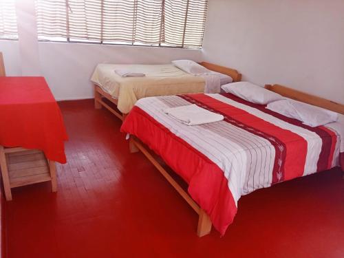 2 Betten in einem Zimmer mit roter und weißer Bettwäsche in der Unterkunft ENEDE HOSTEL in Cusco