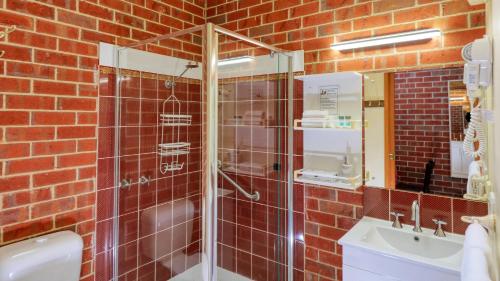 a red brick bathroom with a shower and a sink at Elms Motor Inn in Tumut