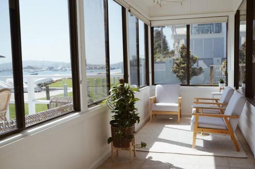 a porch with chairs and a potted plant and windows at Sunset Beach House in Soldiers Point