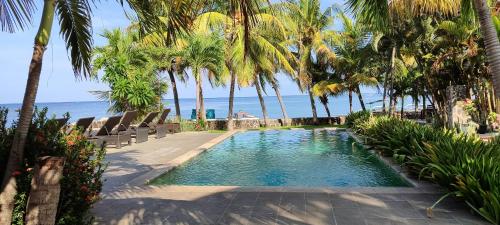 una piscina con palmeras y el océano en 1000 Dream Bungalow en Lovina