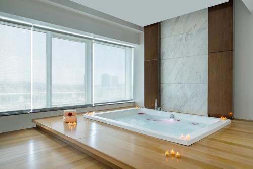 uma grande banheira num quarto com janelas grandes em Riviera Rayhaan by Rotana Doha em Doha
