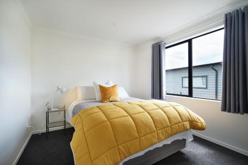 a bedroom with a yellow blanket on a bed with a window at Fabulous River View - Brand New House In Hamilton in Hamilton