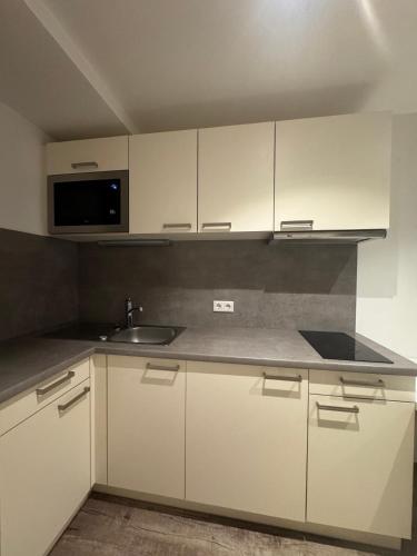a kitchen with white cabinets and a sink and a microwave at SKILL Mountain Lodge - Ski und Bike Hostel im Sommer mit JOKER CARD in Saalbach Hinterglemm