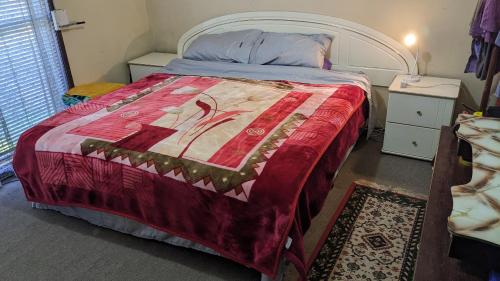 1 dormitorio con 1 cama con manta roja en Homestay - Large Private Room With A King Size Bed - SHARED Bathroom FREE Kitchen Essentials Milk, Bread, Tea, Coffee and Cereal WIFI HDTV FREE Laundry Service Meal and Transportation services available on request, en Bidwill
