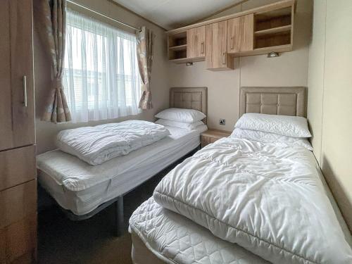 Duas camas num pequeno quarto com uma janela em Beautiful 6 Berth Caravan With Decking At Valley Farm Holiday Park Ref 46736v em Great Clacton