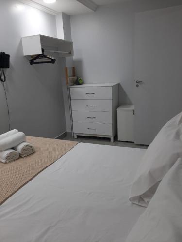 a white bedroom with a bed and a dresser at Apartamento confortável in Goiânia
