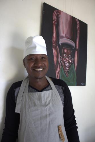 a man wearing a chefs hat standing in front of a painting at KABA Local Rwandan Guesthouse Entire Property for you with Tour services in and out the city such as Safari's in Kigali