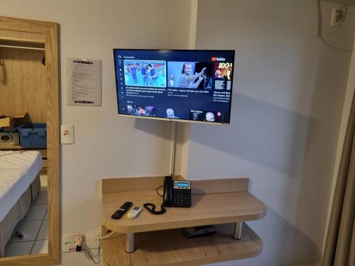 a television on a wall with a phone on a table at Flat 317 Golden Dolphin Express in Caldas Novas