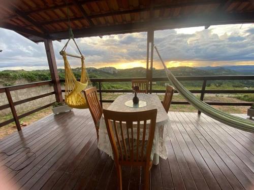 una mesa y sillas en una terraza con hamaca en Chalé Vista Encanto dos Montes, en Monte das Gameleiras
