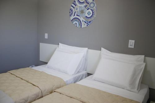 dwa łóżka z białymi poduszkami i talerzem na ścianie w obiekcie Vincenzo Hotel w mieście São Vicente de Minas