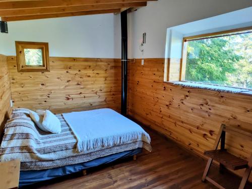 a bedroom with a bed in a wooden room with a window at Cabaña de montaña Ruca Calel in San Carlos de Bariloche