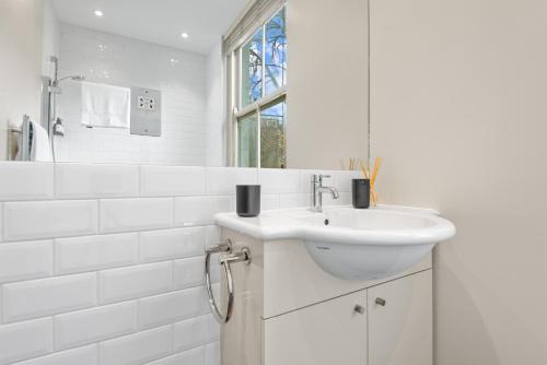 een witte badkamer met een wastafel en een spiegel bij Notting Hill: Stylish 1BR with Terrace - Suite Inn in Londen