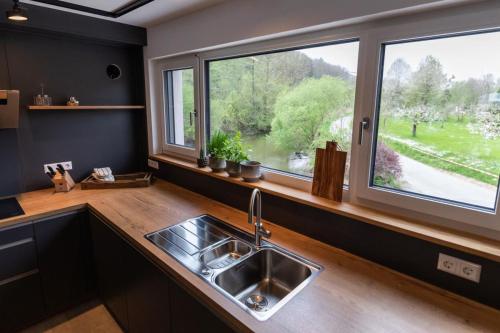 eine Küche mit einem Waschbecken und zwei großen Fenstern in der Unterkunft Freistehendes Ferienhaus Renkenmühle näher kann man am Wasser nicht wohnen in Eberbach