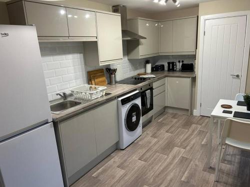 cocina con armarios blancos, lavadora y secadora en Modern Relaxing Apartment en Stoke on Trent