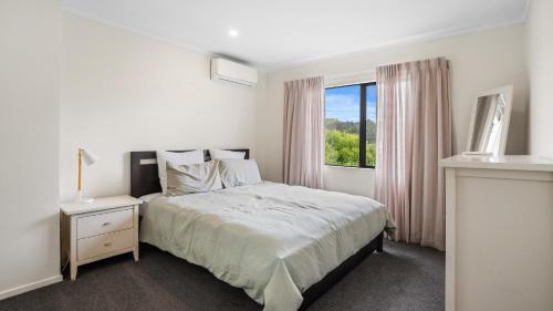 a white bedroom with a bed and a window at Hibiscus Hideaway - Orewa Beach Holiday Home in Orewa