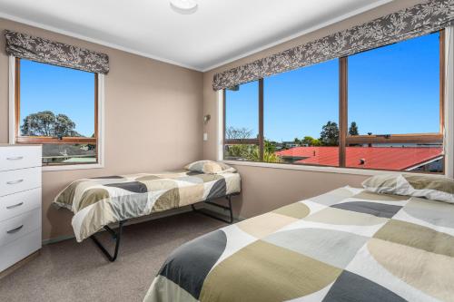 2 camas en un dormitorio con ventanas grandes en Heavenly on Riverside - Whakatāne Holiday Home, en Whakatane