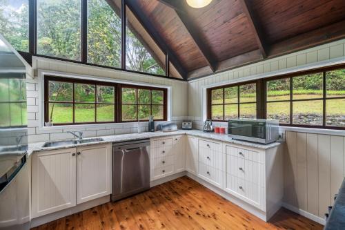 a large kitchen with white cabinets and windows at Cockatoo Hideaway- Cabin in Montville