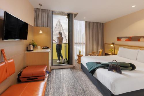 a hotel room with a bed and a woman looking out the window at Brady Hotels Central Melbourne in Melbourne