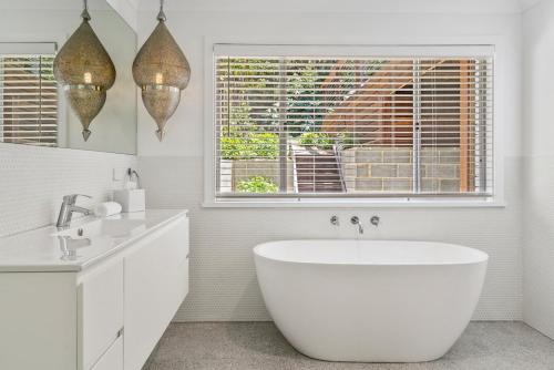 a white bathroom with a tub and a window at The White House at Pearl Beach in Pearl Beach