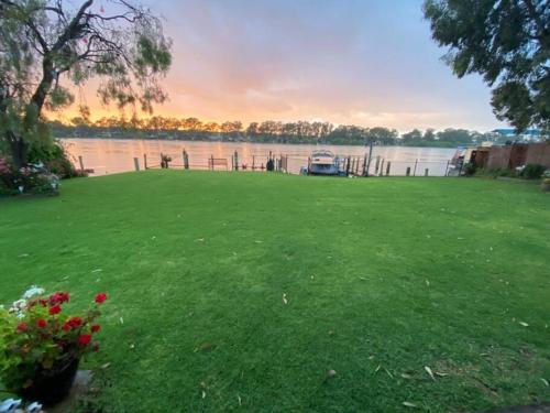 a grassy yard with a boat on the water at 'Bella Vista' in Mannum