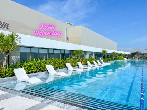 une piscine avec des chaises longues blanches en face d'un hôtel dans l'établissement The Song Luxury Condotel Vung Tau - Xuân's Homestay, à Vung Tau
