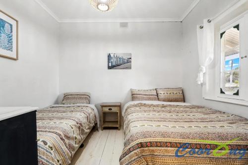 two beds in a room with white walls and a window at Hyde Cottage in Meningie