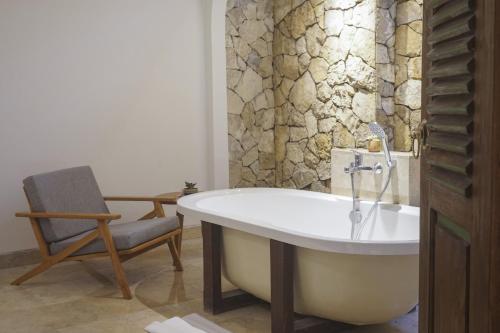 a bathroom with a bath tub and a chair at Motama Villa in Ubud