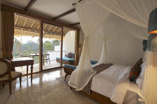 a bedroom with a bed with a hammock and a desk at Motama Villa in Ubud