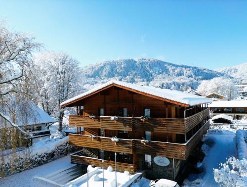 a log cabin in the snow with mountains in the background at Hotel Villa Lago Garni in Bad Wiessee