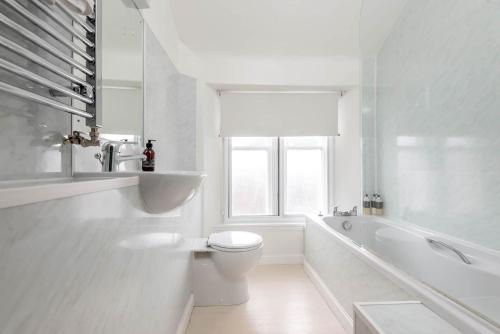 a white bathroom with a toilet and a bath tub at Park Place Elie, Perfect for the beach in Elie