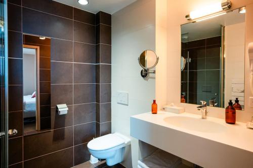 W łazience znajduje się umywalka, toaleta i lustro. w obiekcie Hôtel de la Plage w mieście Excénevex