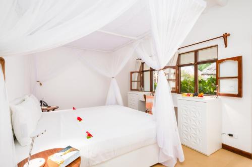 a white bedroom with a bed and a table at Sandies Baobab Beach Zanzibar in Nungwi