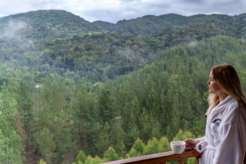 a woman standing on a railing with a cup of coffee at Gorilla Leisure Lodge in Kisoro