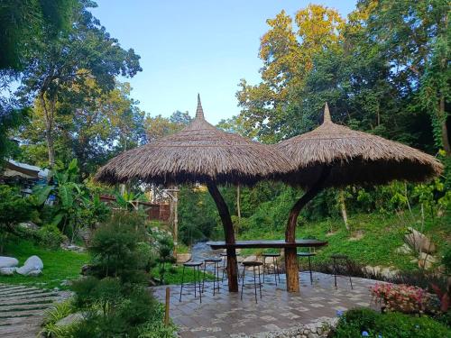 a picnic table with a straw umbrella and chairs at Lhong Chiang Dao Glamping หลงเชียงดาว in Chiang Dao